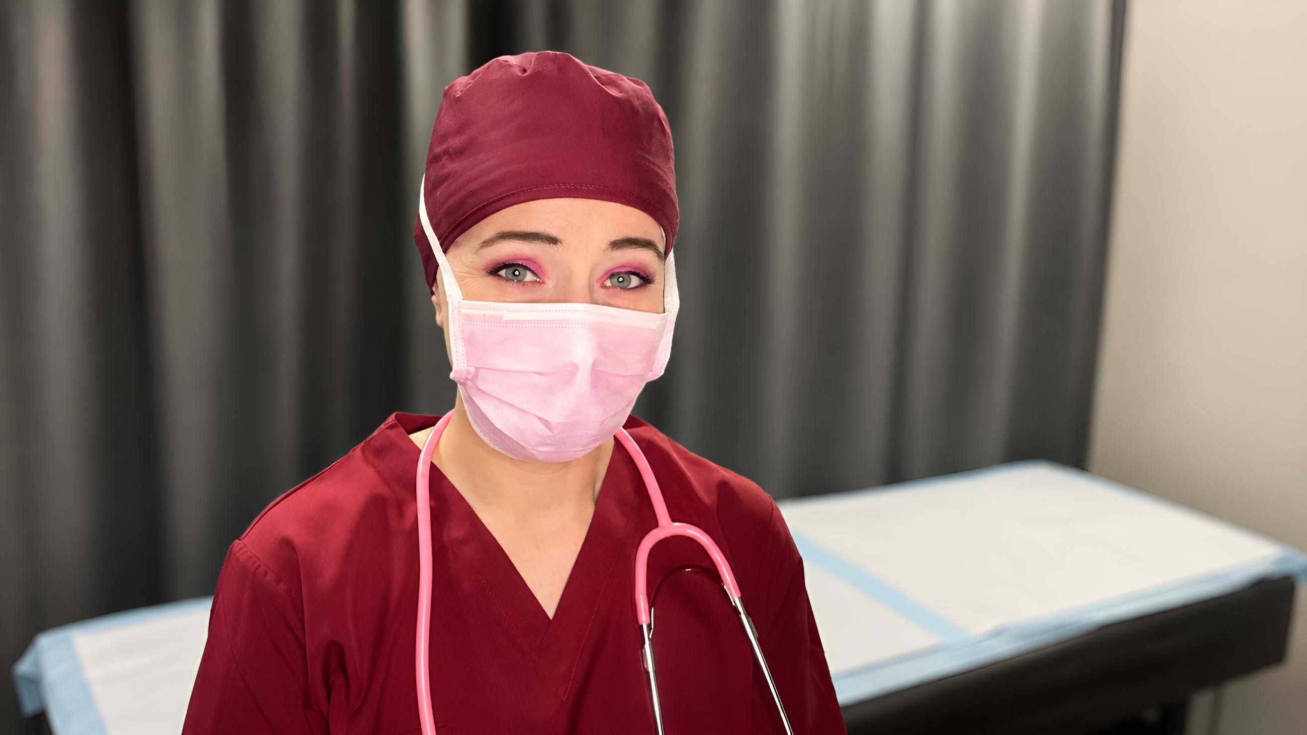 Miss Nena Belgium in maroon scrubs preparing the clinical area for a specialized medical BDSM experience